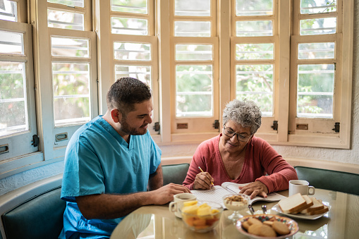 Mid adult nurse and senior woman playing with crosswords on breakfast at home