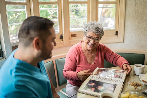 Senior woman and mid adult nurse looking at photo album in the dining room in a nursing home