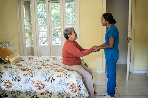 Mid adult nurse helping senior woman rise up of bed at nursing home