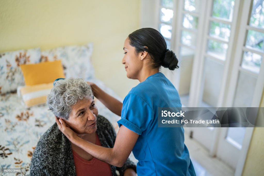 Mid adult nurse combing senior woman's hair in bedroom at nursing home Geriatrics Stock Photo