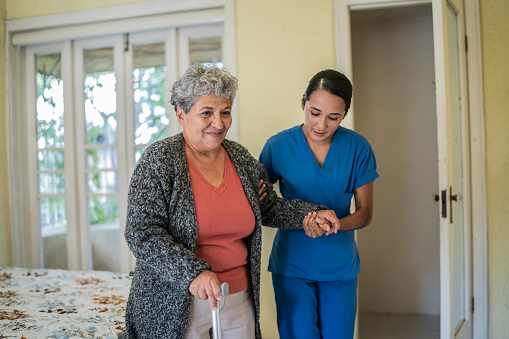 Mid adult nurse helping senior woman walk at nursing home