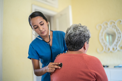 Enfermera mediana de adultos que examina los pulmones de una mujer mayor con estetoscopio en el dormitorio de un hogar de ancianos photo