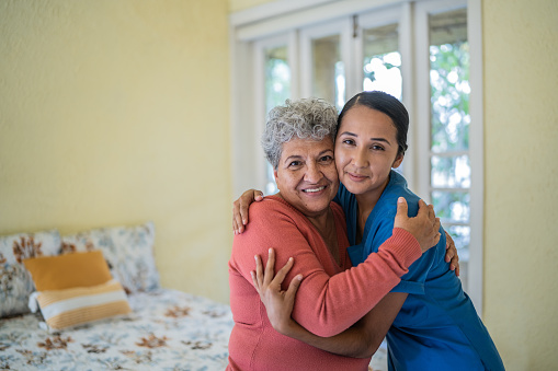 Portrait of mid adult nurse embracing senior woman in the bedroom at home