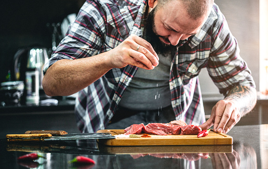 Middle aged man with beard preparing fresh sliced beef meat in the kitchen