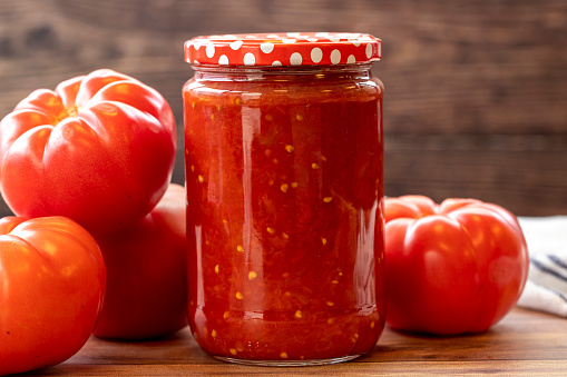 Canned tomato sauce in glass jar on wood background