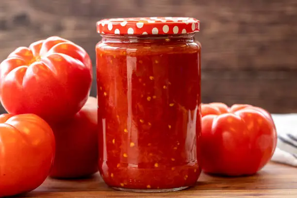 Photo of Canned tomato sauce in glass jar on wood background