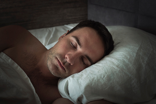 Handsome young man sleeping in white bedding. Head close-up on a pillow while sleeping at night.