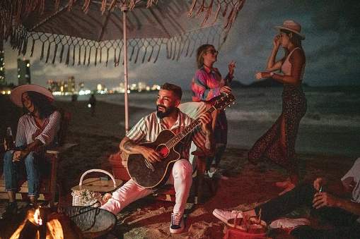 Mid adult man playing acoustic guitar to his friends on the beach