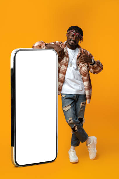 istock Smiling african man standing near huge smartphone with blank screen on yellow studio background 1435021781
