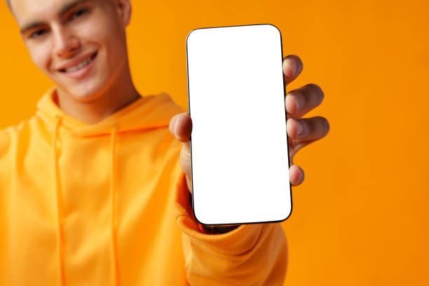 istock Smiling young man showing mobile phone blank white screen on yellow background 1435021787