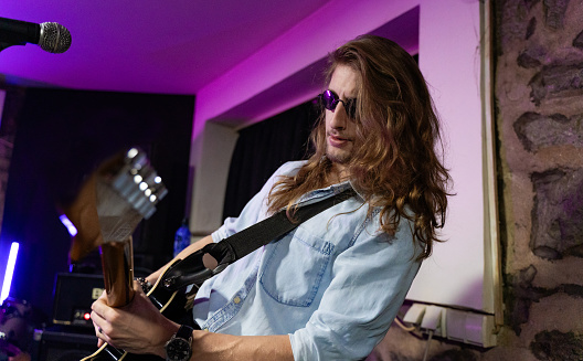 Caucasian ethnicity Young adult man with long hair, playing electric guitar in studio