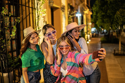 Female friends taking a selfie on mobile phone outdoors at night