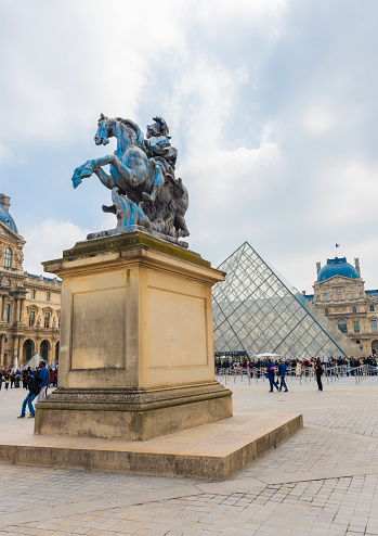 A lot of tourists walk in square of Louvre Museum Pyramid in Paris, France