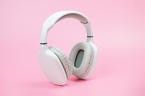 White wireless on-ear headphones on pink background. Headphones with ear cushions made of soft and pleasant to the touch material for playing games and listening to music tracks