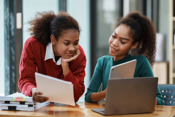 Focused young african american businesswoman or student looking at laptop holding book learning, serious black woman working or studying with computer doing research or preparing for exam online Focused young African American businesswoman or student looking at laptop holding book learning, serious black woman working or studying with computer doing research or preparing for exam online high school student classroom education student stock pictures, royalty-free photos & images