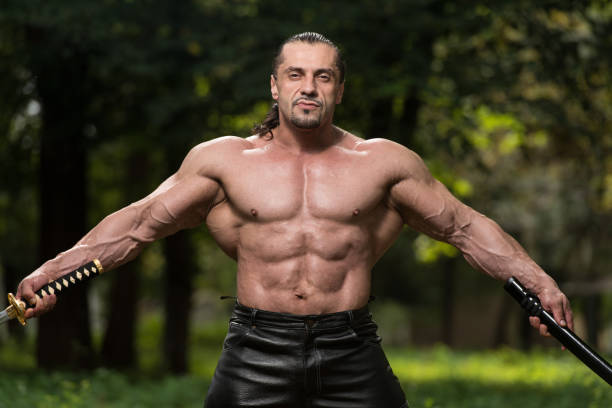 Action Hero Muscled Man Holding A Ancient Sword - Standing In Forest Wearing Leather Pants