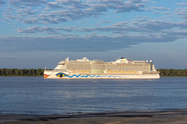 Stade, Germany – August 7, 2022: Cruise ship AIDAPerla, owned by Carnival Corporation, leaving Hamburg on Elbe river at dusk