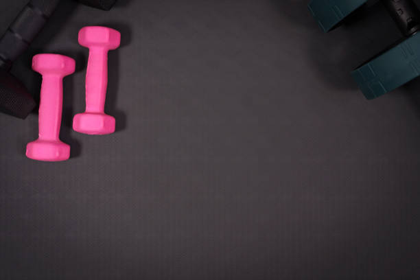 istock Pink and black dumbbell background with the abdominal roller on black rubber background.fitness equipment background concept 1435046118