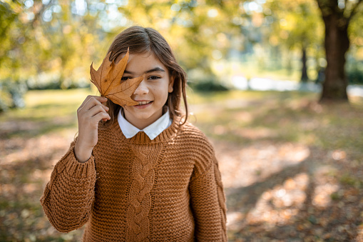 Smiling girl hiding her face behind an autumn maple leaf