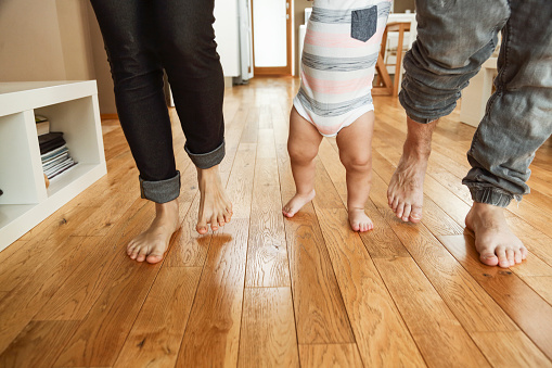 First steps of a child with the parents helping. All barefoot on hardwood floor. What a joy.....