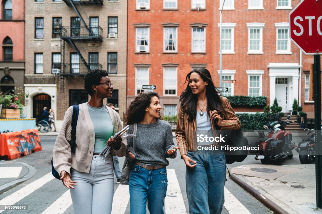 Three friends are walking together in the street - Gay St, New York City, USA Three friends are walking together in the street - Gay St, New York City, USA. They are going to school together. New York City Stock Photo