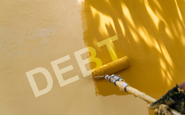 istock Hand sweeping the word debt on yellow wall with paint roller 1435050150