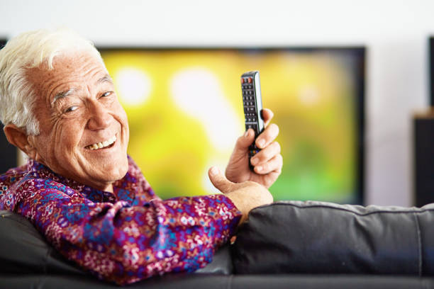 istock Handsome elderly man laughs cheerfully as he holds his TV remote control. 1435055094
