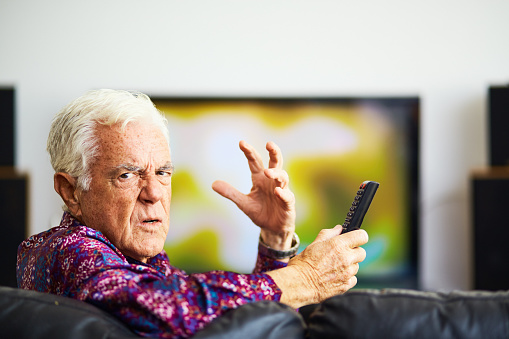Good-looking senior man in patterned open-neck shirt looks very cross about something that's gone wrong with his television viewing.