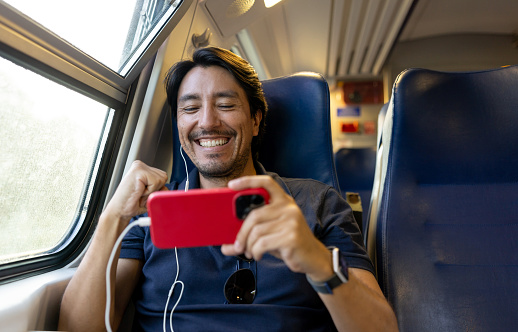 Happy man riding on the train and watching a soccer game on his cell phone using headphones