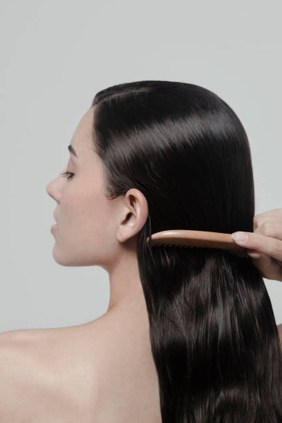 Beautiful brunette woman brushing her hair Shiny healthy simple hairstyle Long dark brown wavy almost straight Hair Fashion model studio portrait on light gray background Close-up headshot back view Perfect for Shampoo Hair care treatment conditioner advertising ad campaign Make your hair super shiny and healthy impression hermosa mujer morena cepillándose el cabello brillante saludable peinado simple largo marrón oscuro ondulado casi liso cabello modelo de moda retrato de estudio sobre fondo gris claro primer plano vista trasera champú anuncio de tratamiento para el cuid