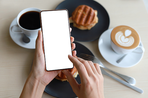 Cropped shot of female hand holding a blank screen phone in a cafe, high angle image.