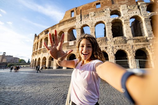 Happy female tourist making a video call from the Coliseum in Rome - travel concepts