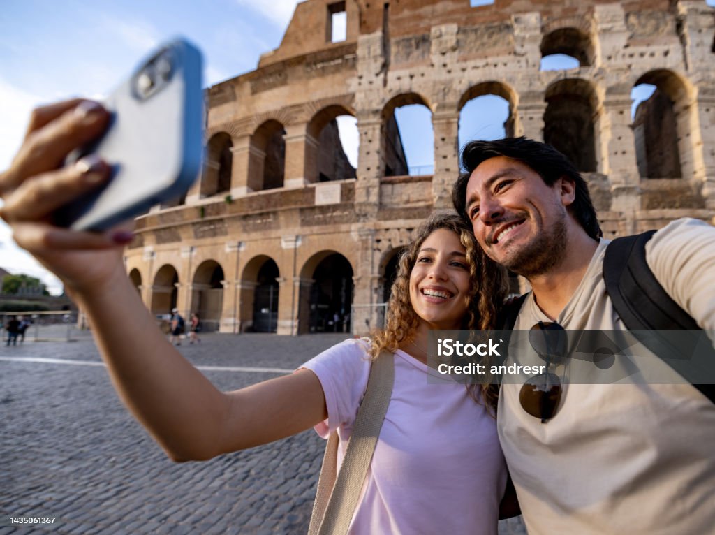 Happy couple of travelers in Rome taking a selfie with the Coliseum Happy couple of travelers in Rome taking a selfie with the Coliseum using a cell phone - traveling concepts Tourism Stock Photo
