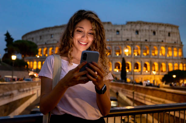 happy tourist in rome visiting the coliseum and texting on her phone - rome coliseum night famous place imagens e fotografias de stock