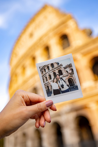 Happy couple of tourists taking a photo at the Roman Coliseum with an instant camera - traveling concepts