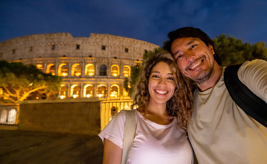 Happy couple of tourists in Rome taking a selfie with the Coliseum at nighttime  - traveling concepts