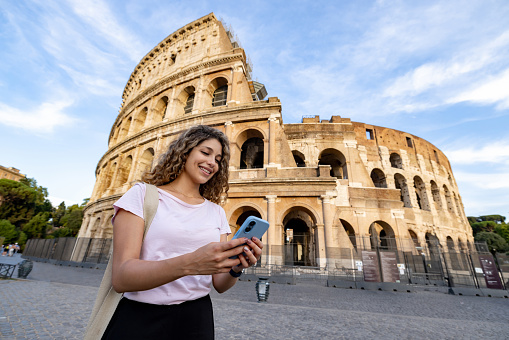 Happy tourist at the Coliseum in Rome using a mobile app on her cell phone - travel concepts