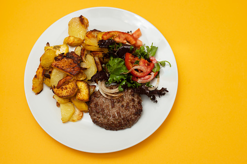 three fried ground meat with fried potato and fresh salad on the plate on yellow