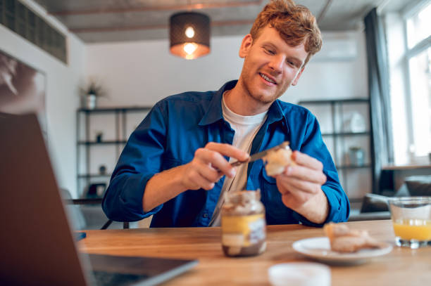 istock Ginger young man sitting in th kitchen and making sandwich with chocolate paste 1435061773