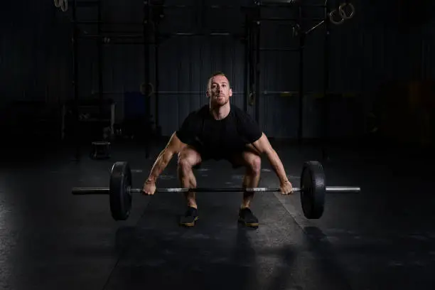 Male athlete in box gym environment performing a barbell snatch