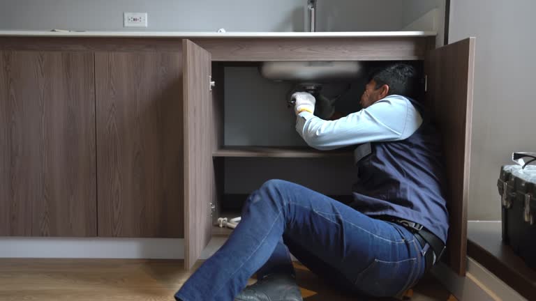 Latin American plumber using a wrench to fix a leaking pipe in the kitchen sink