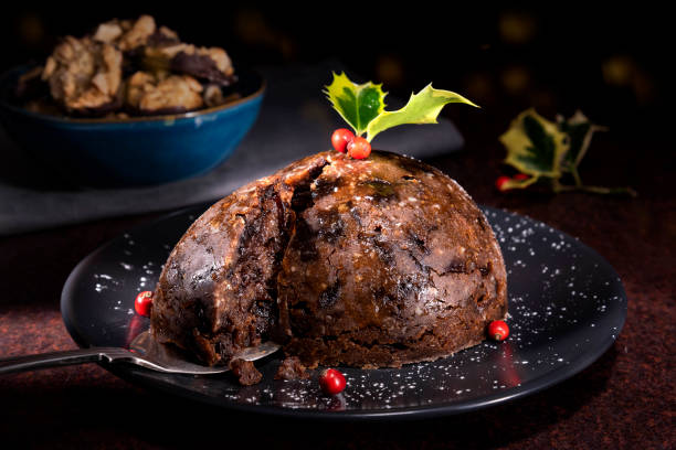 Christmas pudding in the foreground with mince pies and Florentine biscuits in the background - stock photo Christmas pudding on a plate in the foreground. There is holly with berries at the top of the Christmas pudding.  Mince pies and Florentine biscuits are placed in the background. christmas pudding stock pictures, royalty-free photos & images