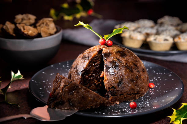 Christmas pudding in the foreground with mince pies and Florentine biscuits in the background - stock photo Christmas pudding on a plate in the foreground. There is holly with berries at the top of the Christmas pudding.  Mince pies and Florentine biscuits are placed in the background. christmas pudding stock pictures, royalty-free photos & images