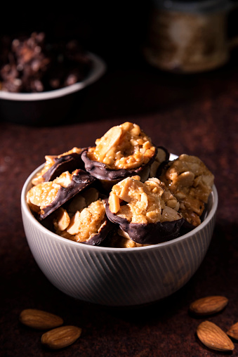 Chocolate Florentines cookies with almond in the foreground. The Chocolate Florentines is placed in a ceramic bowl. The photograph is dark and moody.
