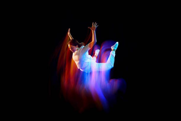Creative dynamic portrait of athlete, dancer in white sports clothes jumping, flying over dark background in mixed neon light, glow. Art, aspiration, music, fashion Creative dynamic portrait of athlete, dancer in white sports clothes jumping, flying over dark background in mixed neon light, glow. Art, aspiration, music, fashion. Copy space for ad levitation stock pictures, royalty-free photos & images