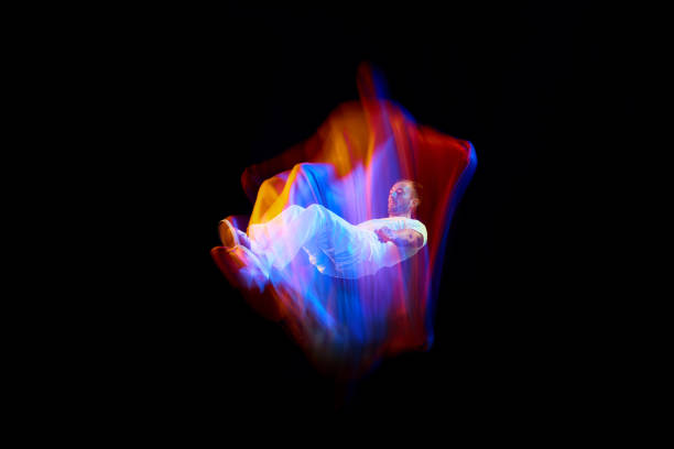 Dance in motion. Studio shot of flying, jumping dancer or gymnast performing tricks in the air over black background with mixed neon glowing rays Dance in motion. Studio shot of flying, jumping dancer or gymnast performing tricks in the air over black background with mixed neon glowing rays. Fantasy, cyberpunk, sport, fashion hyperdrive stock pictures, royalty-free photos & images