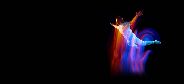 Dance in motion. Studio shot of flying, jumping dancer or gymnast performing tricks in the air over black background with mixed neon glowing rays Dance in motion. Studio shot of flying, jumping dancer or gymnast performing tricks in the air over black background with mixed neon glowing rays. Fantasy, cyberpunk, sport, fashion hyperdrive stock pictures, royalty-free photos & images