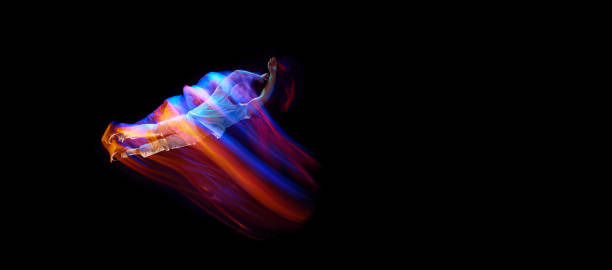 Dance in motion. Studio shot of flying, jumping dancer or gymnast performing tricks in the air over black background with mixed neon glowing rays Dance in motion. Studio shot of flying, jumping dancer or gymnast performing tricks in the air over black background with mixed neon glowing rays. Fantasy, cyberpunk, sport, fashion. Flyer hyperdrive stock pictures, royalty-free photos & images