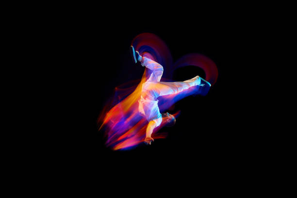 Dance in motion. Studio shot of flying, jumping dancer or gymnast performing tricks in the air over black background with mixed neon glowing rays Dance in motion. Studio shot of flying, jumping dancer or gymnast performing tricks in the air over black background with mixed neon glowing rays. Fantasy, cyberpunk, sport, fashion hyperdrive stock pictures, royalty-free photos & images
