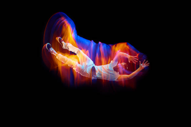 Dance in motion. Studio shot of flying, jumping dancer or gymnast performing tricks in the air over black background with mixed neon glowing rays Dance in motion. Studio shot of flying, jumping dancer or gymnast performing tricks in the air over black background with mixed neon glowing rays. Fantasy, cyberpunk, sport, fashion hyperdrive stock pictures, royalty-free photos & images